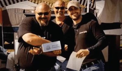 Three men are standing next to each other holding a piece of paper.