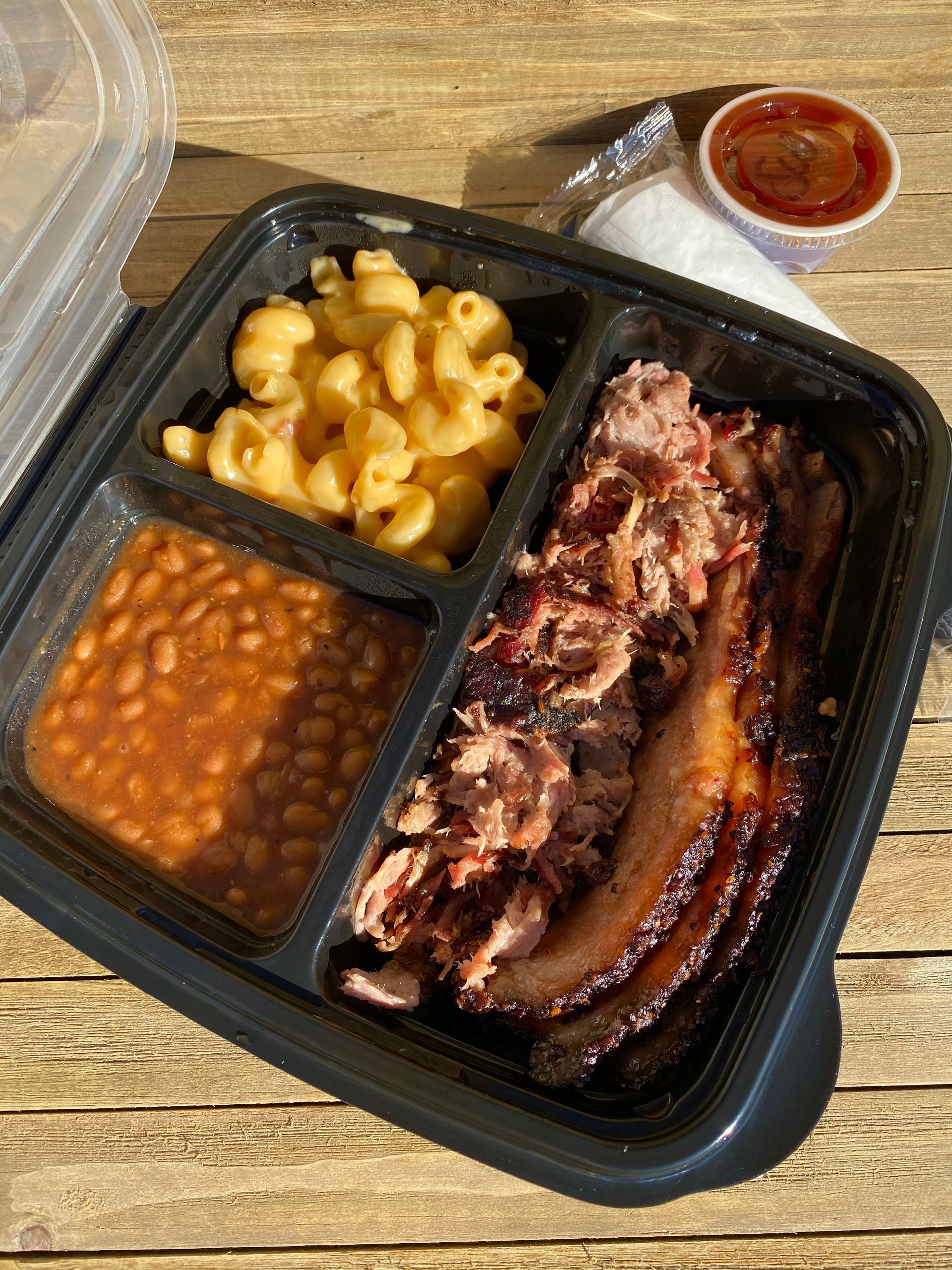 A plastic container filled with meat , macaroni and cheese , beans and sausage.