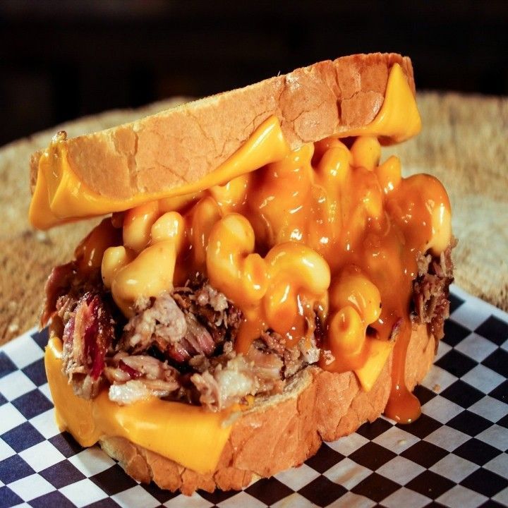 A sandwich with macaroni and cheese on a checkered paper.