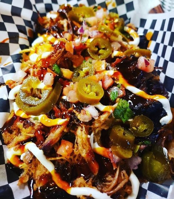 A close up of a plate of BBQ nacho on a checkered paper.