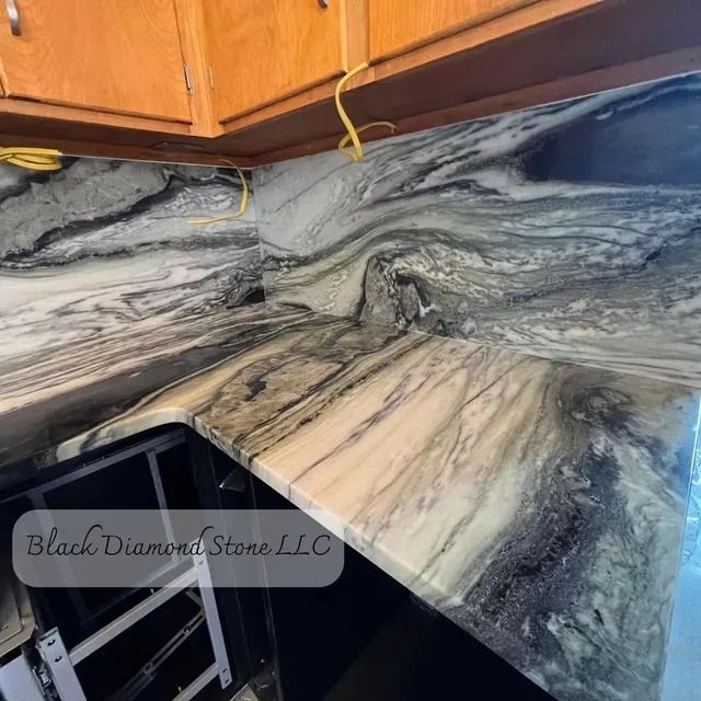 Marble countertop with swirling gray, black, and white patterns, under wooden cabinets; 