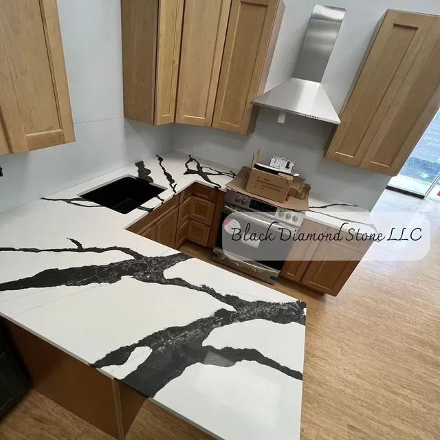 White kitchen countertop with dramatic black veining, oak cabinets, and stainless steel range hood.