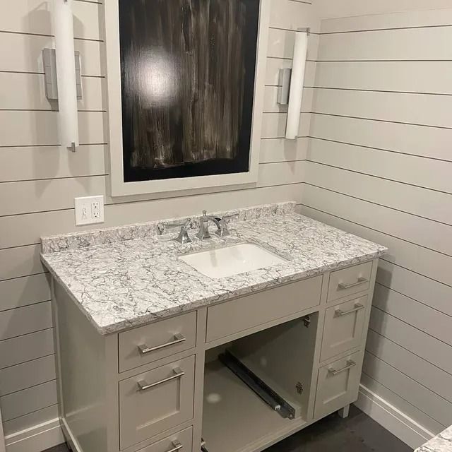 Bathroom vanity with gray countertop, white sink, and artwork; shiplap walls.