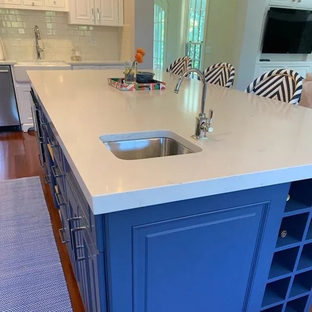 Blue kitchen island with a white countertop and a small sink, in a kitchen.