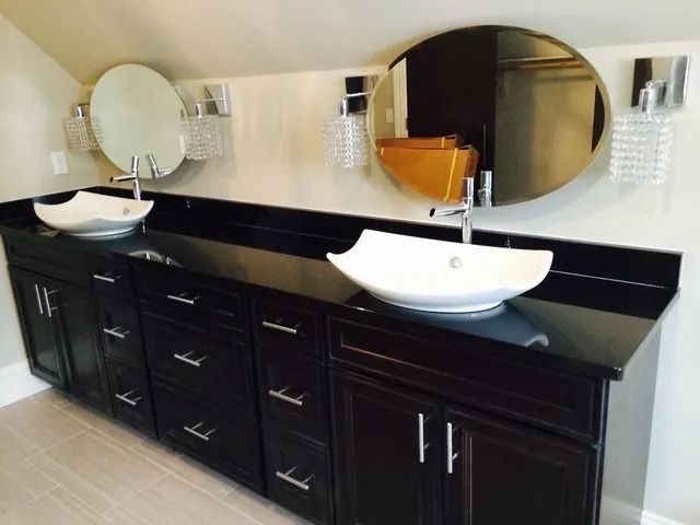 Dark wood double vanity with white vessel sinks, black countertop, and round mirrors.
