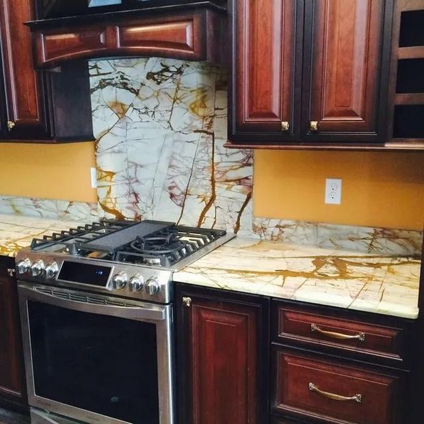 Kitchen with dark wood cabinets, stainless steel range, and gold-veined marble countertops and backsplash.