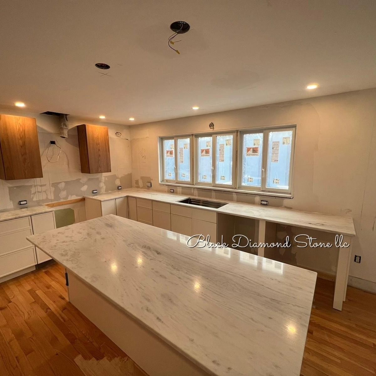 Kitchen under construction with white cabinets, marble countertops, and a wooden floor.