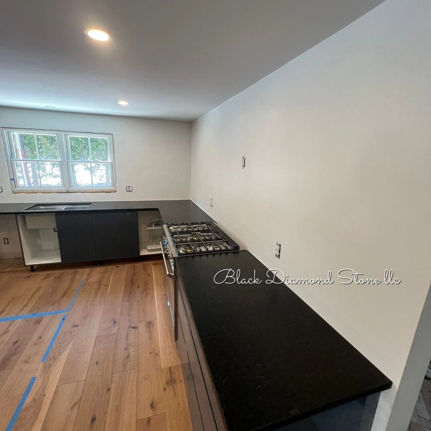 Kitchen remodel in progress: dark countertops, cabinets, gas range, wood floor, white walls, and a window.
