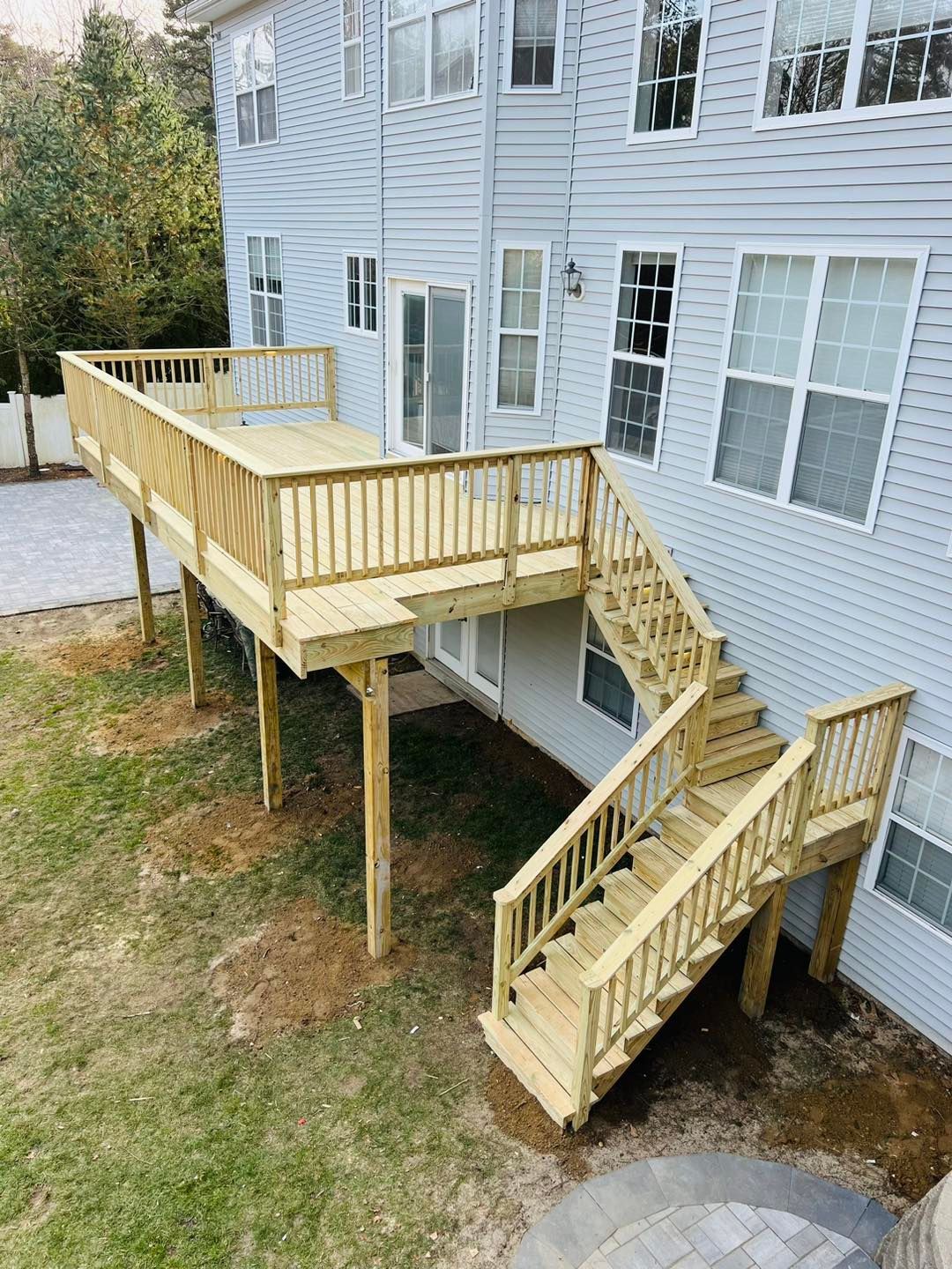 A large wooden deck with stairs leading up to it is in front of a house.