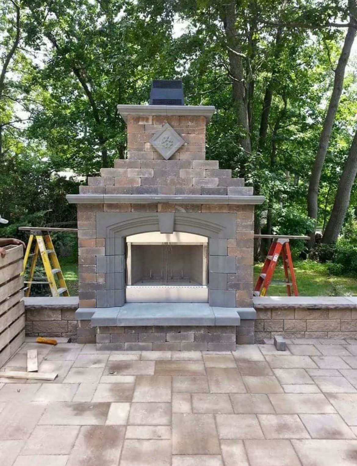 A brick fireplace is being built on a patio with trees in the background.