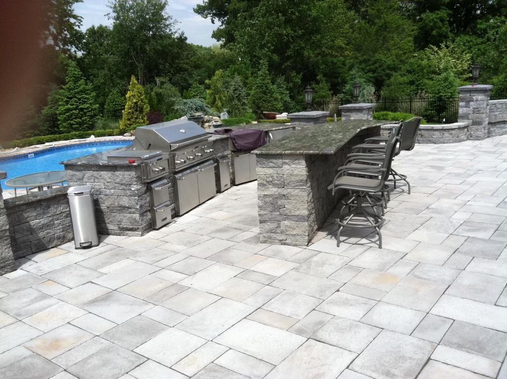 A patio with a grill and a table in front of a pool.