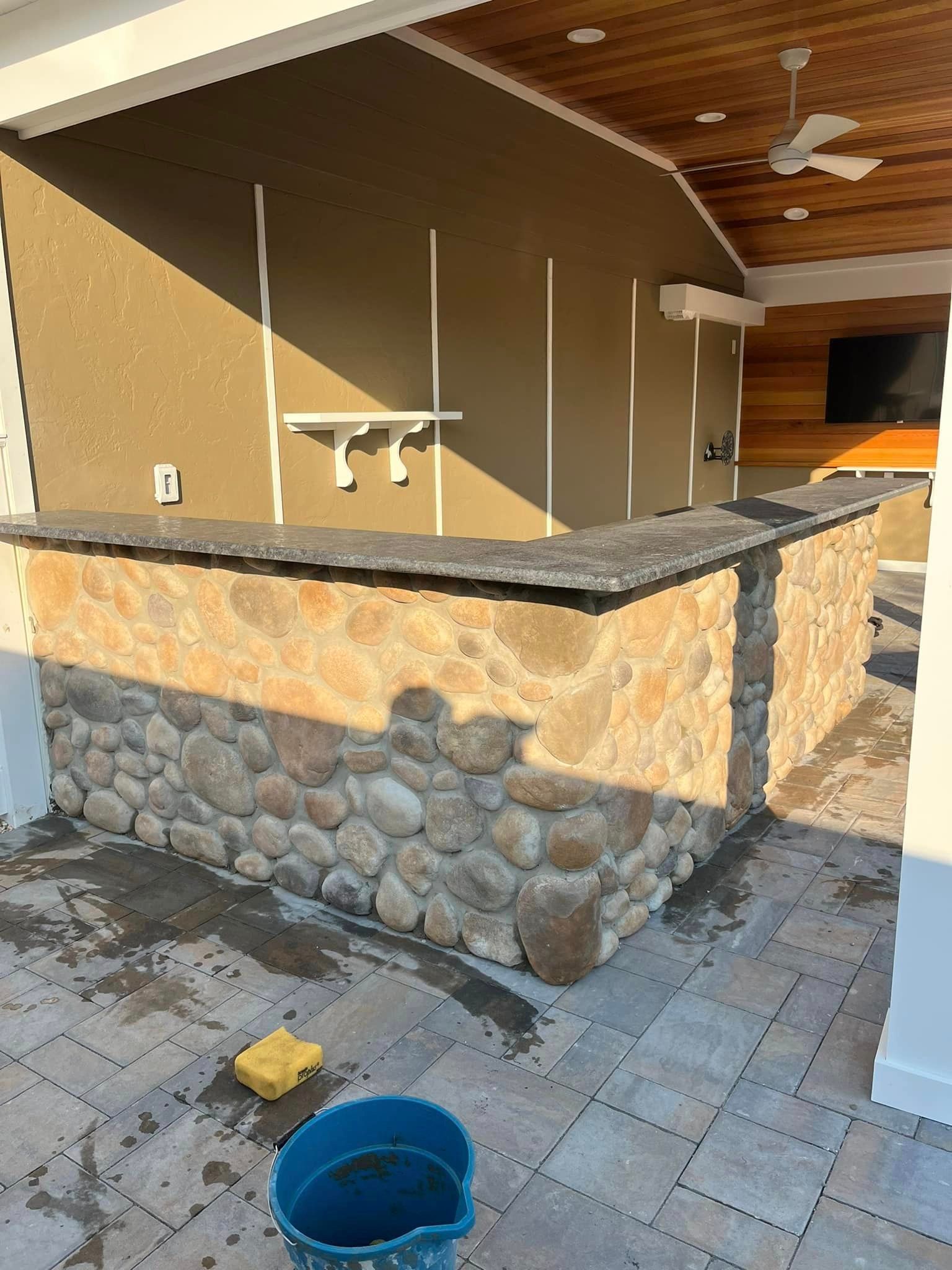 A blue bucket is sitting on the ground next to a stone wall.