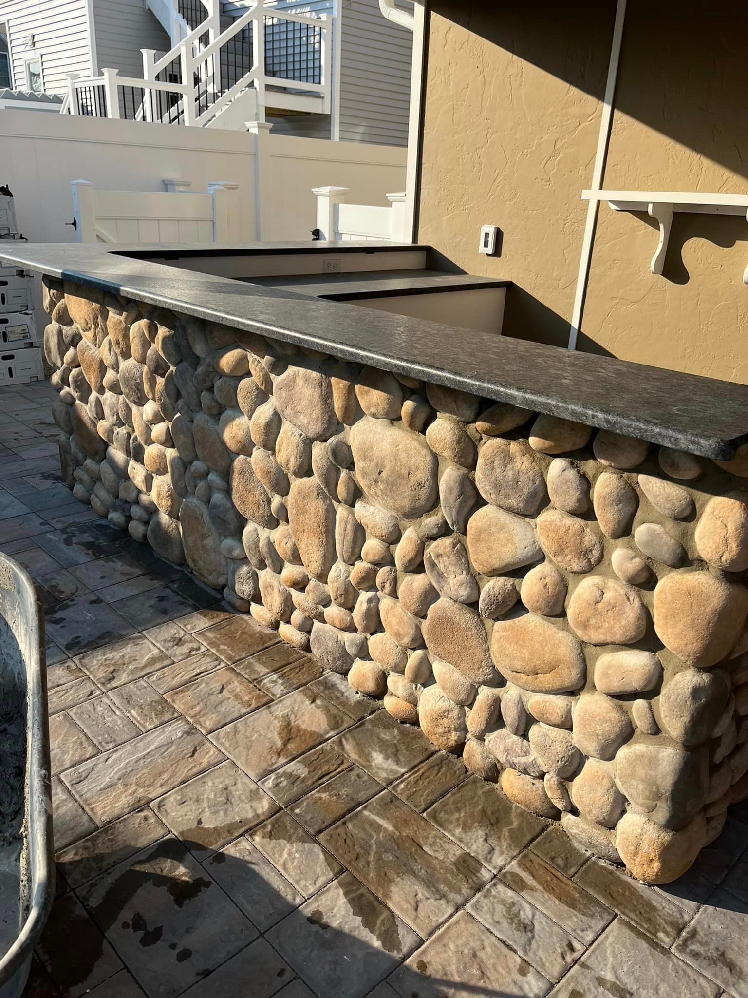 A stone wall with a black counter top is sitting on a brick patio.