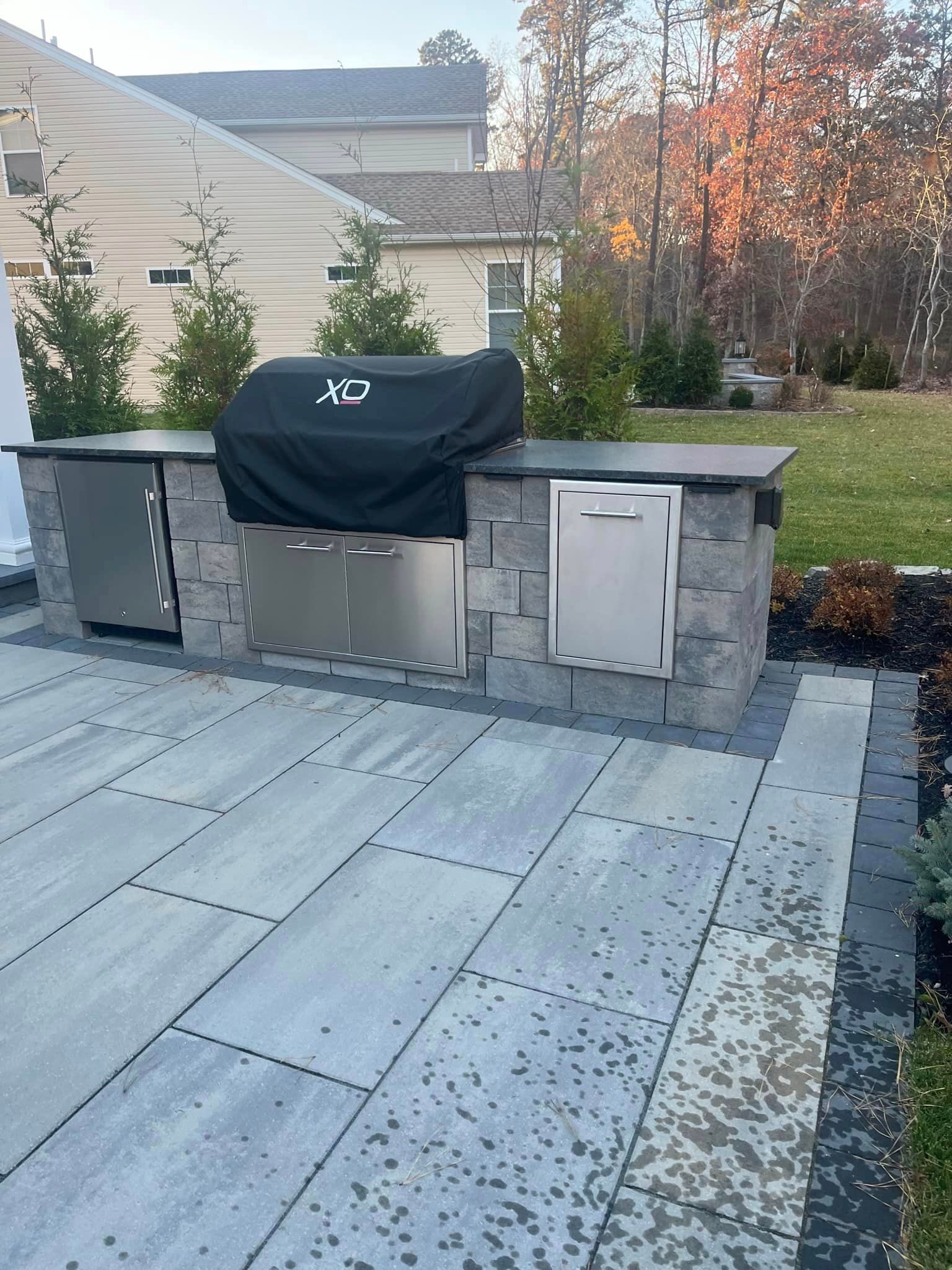 A grill is sitting on top of a patio next to a house.