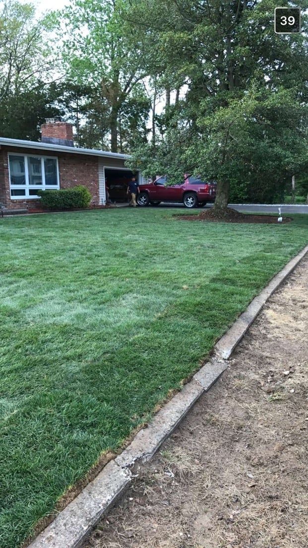 A red car is parked in the driveway of a house next to a lush green lawn.