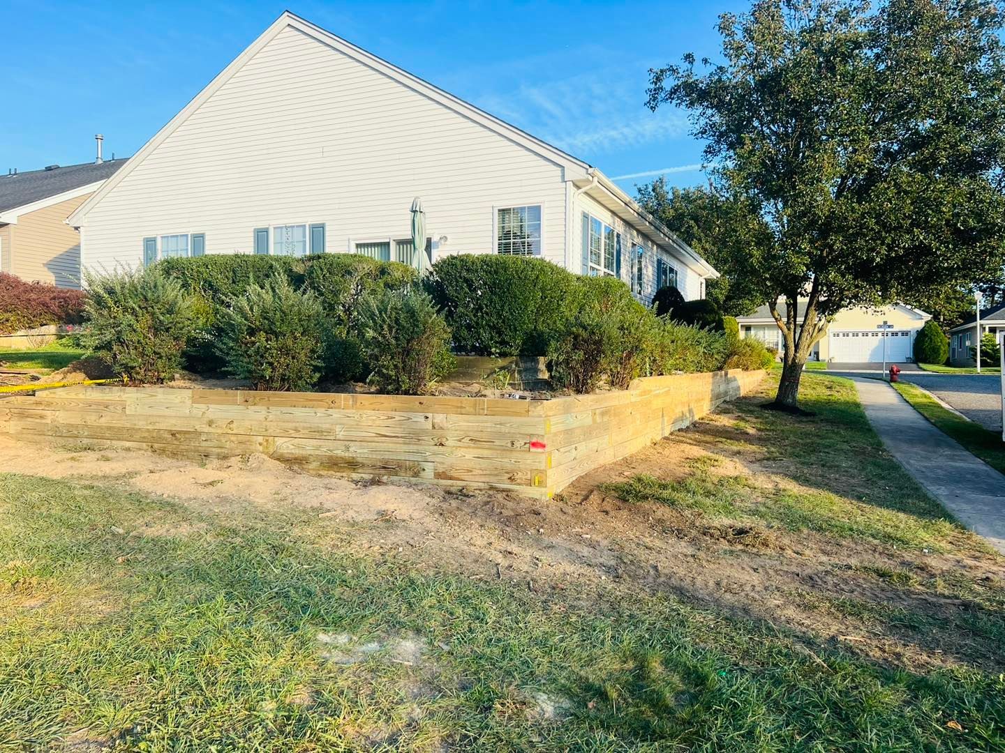 A white house with a wooden retaining wall in front of it.