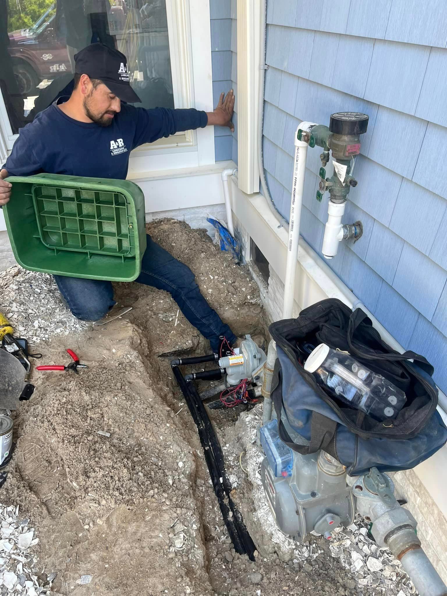 A man is kneeling down in front of a house holding a green box.