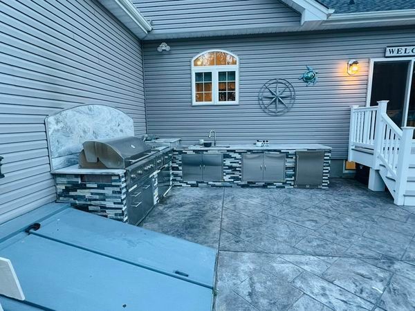 A patio with a grill , sink , and stairs in front of a house.