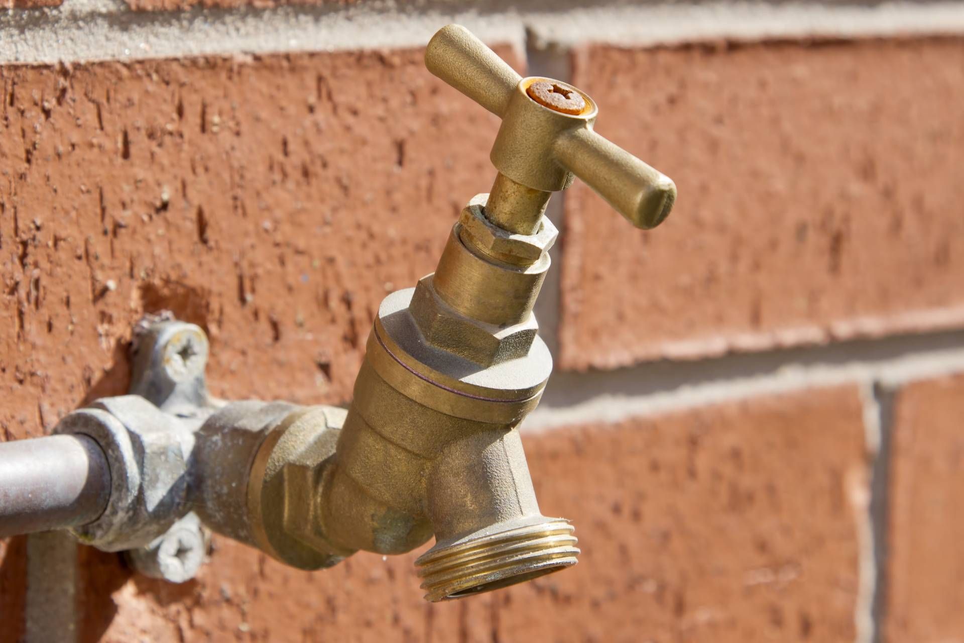 A brass outdoor water spigot mounted on a red brick wall.