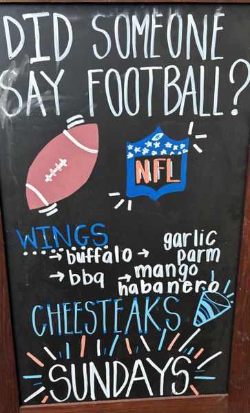 Blackboard sign with football, NFL logo, wing flavors, cheesesteaks, and Sundays.