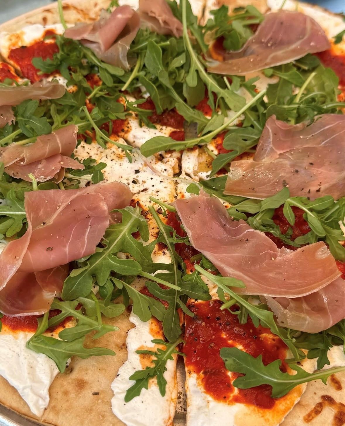 Pizza topped with arugula, prosciutto, and red sauce.