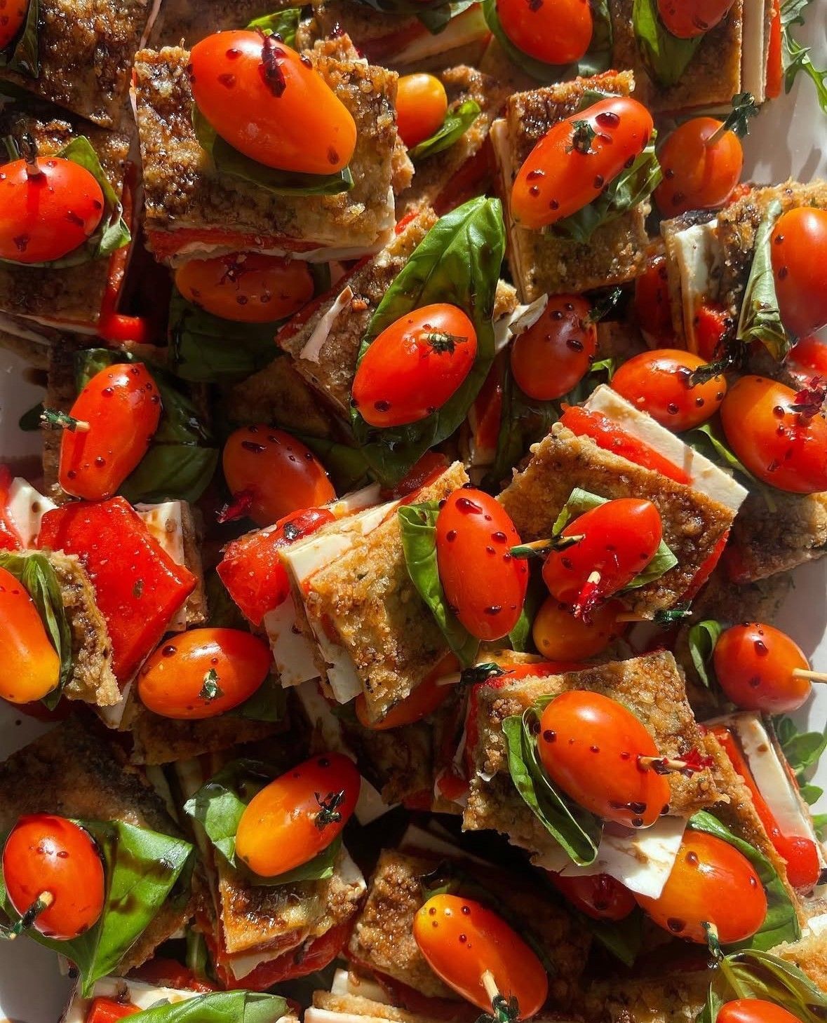 Close-up of numerous small, layered sandwiches topped with grilled tomatoes.