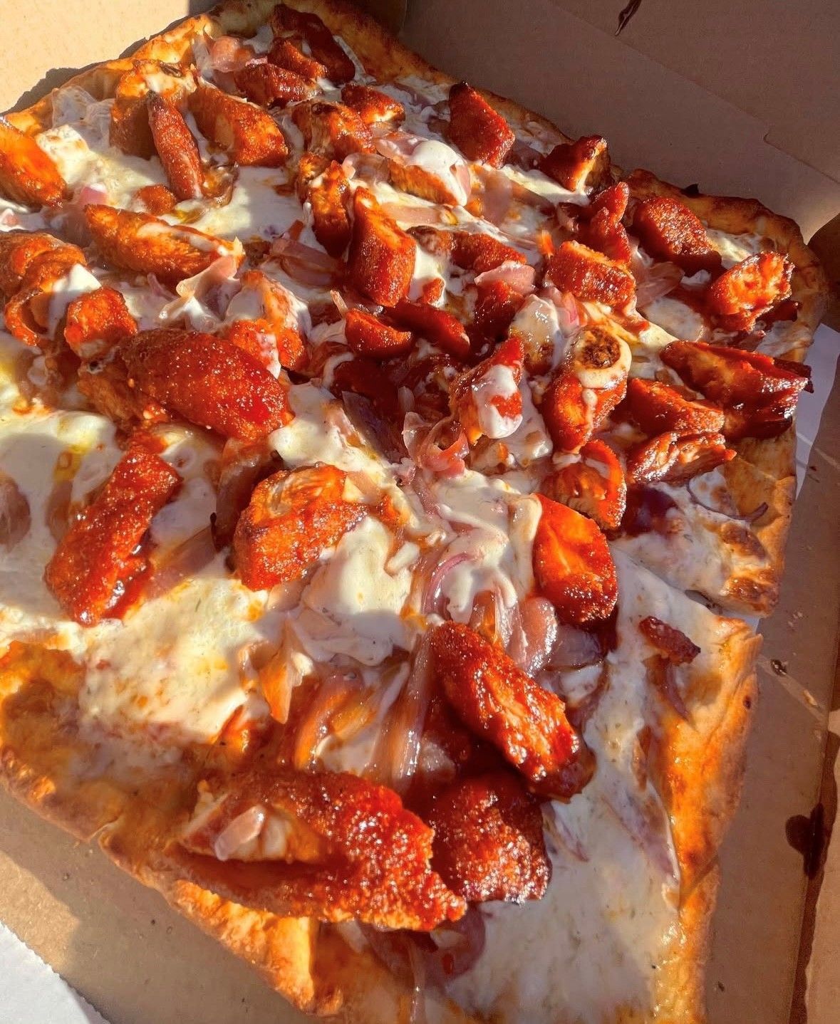 Square pizza with chicken topping, white sauce, and onions.