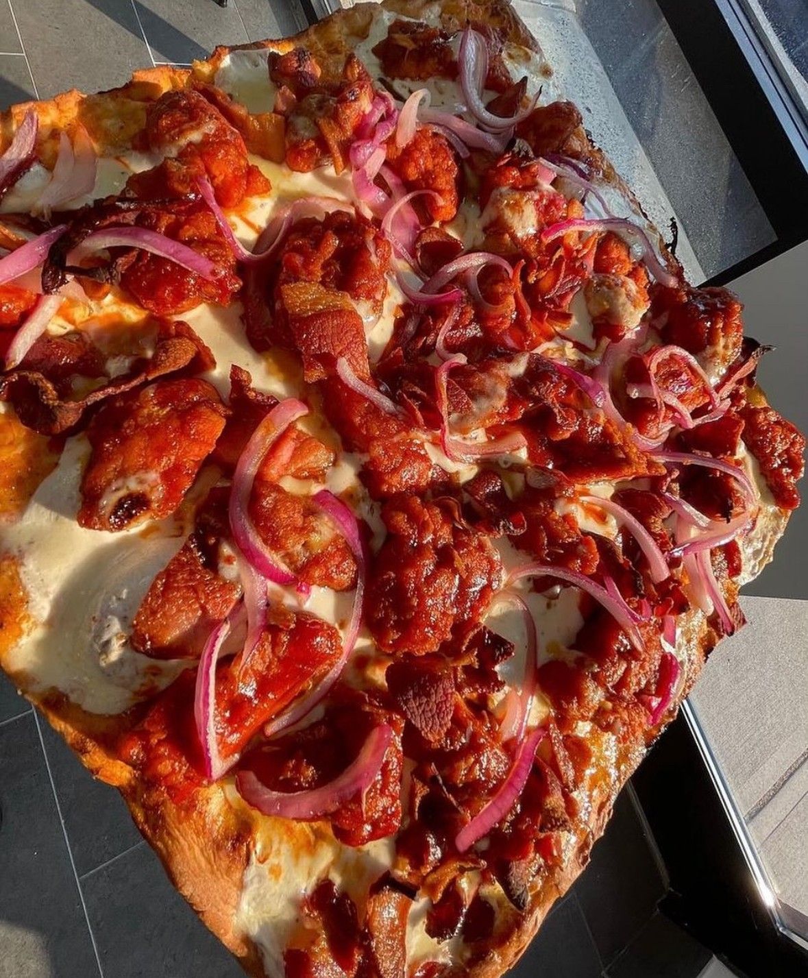 Square pizza topped with red chicken, red onions, and cheese.
