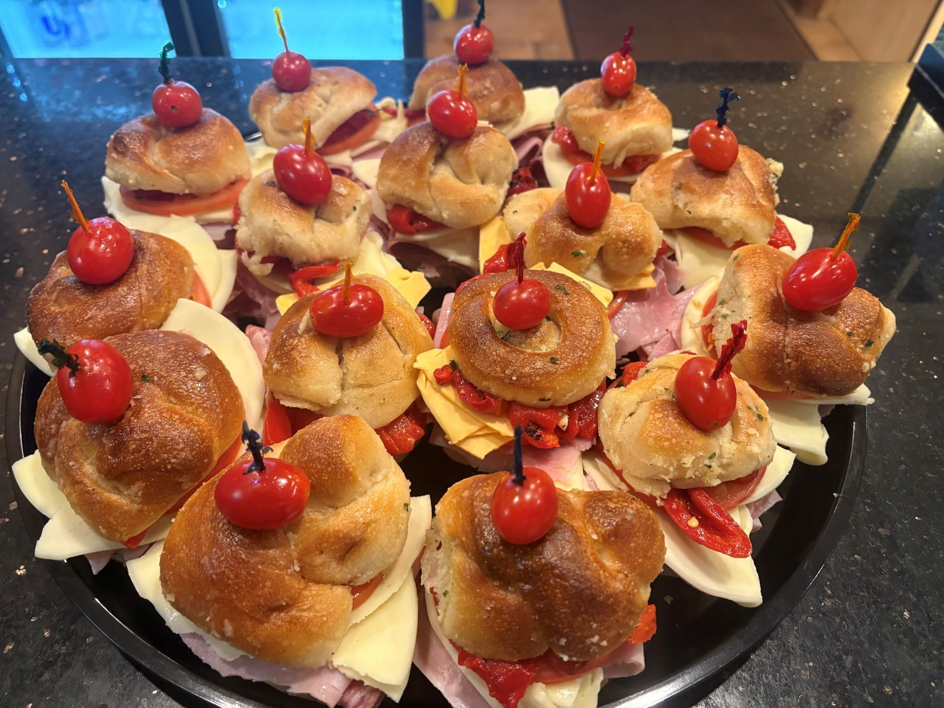 Tray of mini sandwiches, each topped with a cherry and a toothpick.