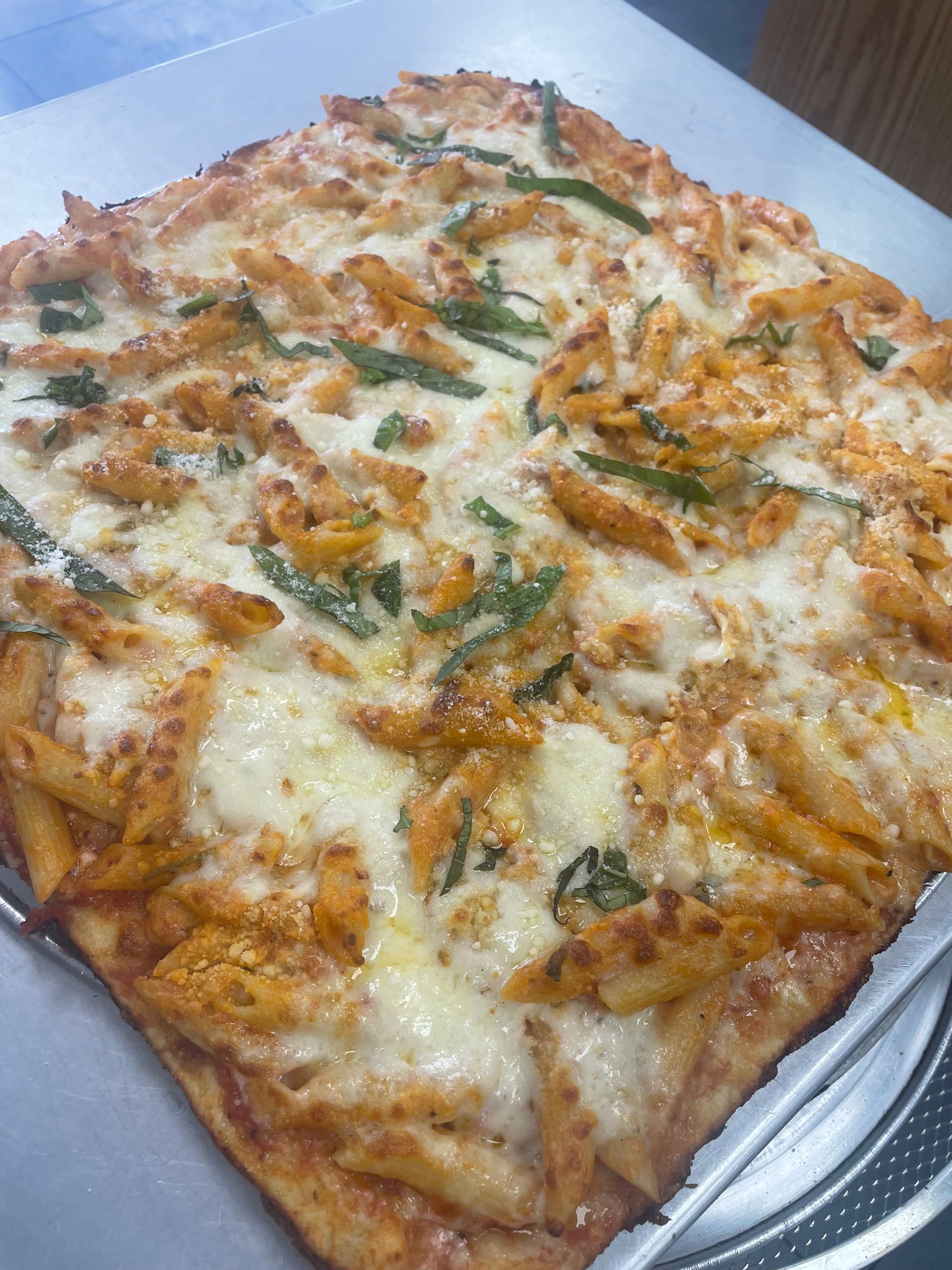 A pizza with pasta and cheese is sitting on a pan on a table.