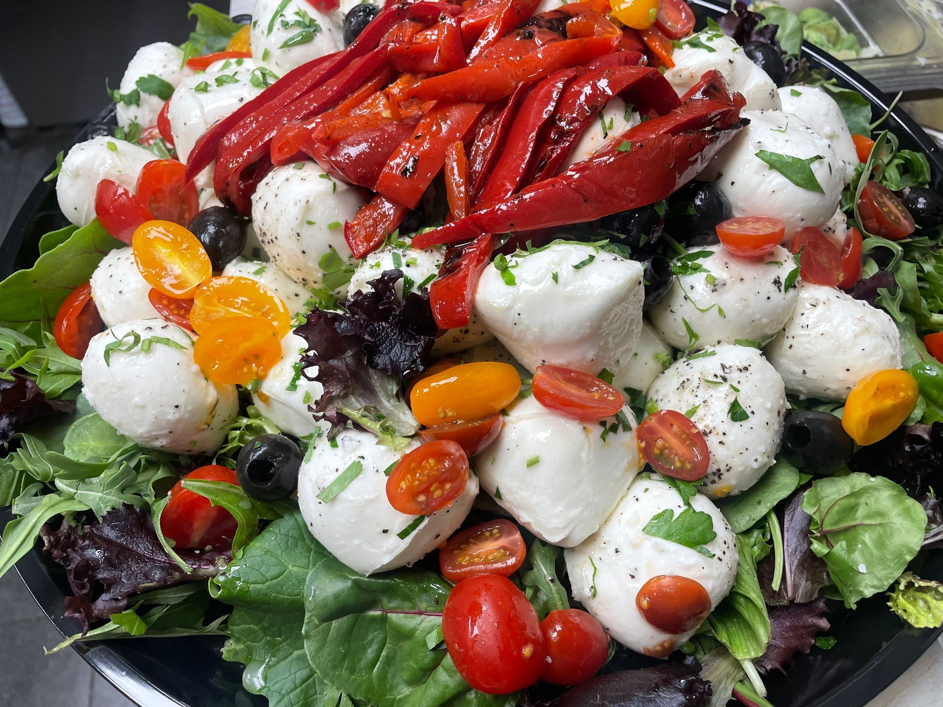 A salad with mozzarella balls, tomatoes, olives, and peppers on a black plate.