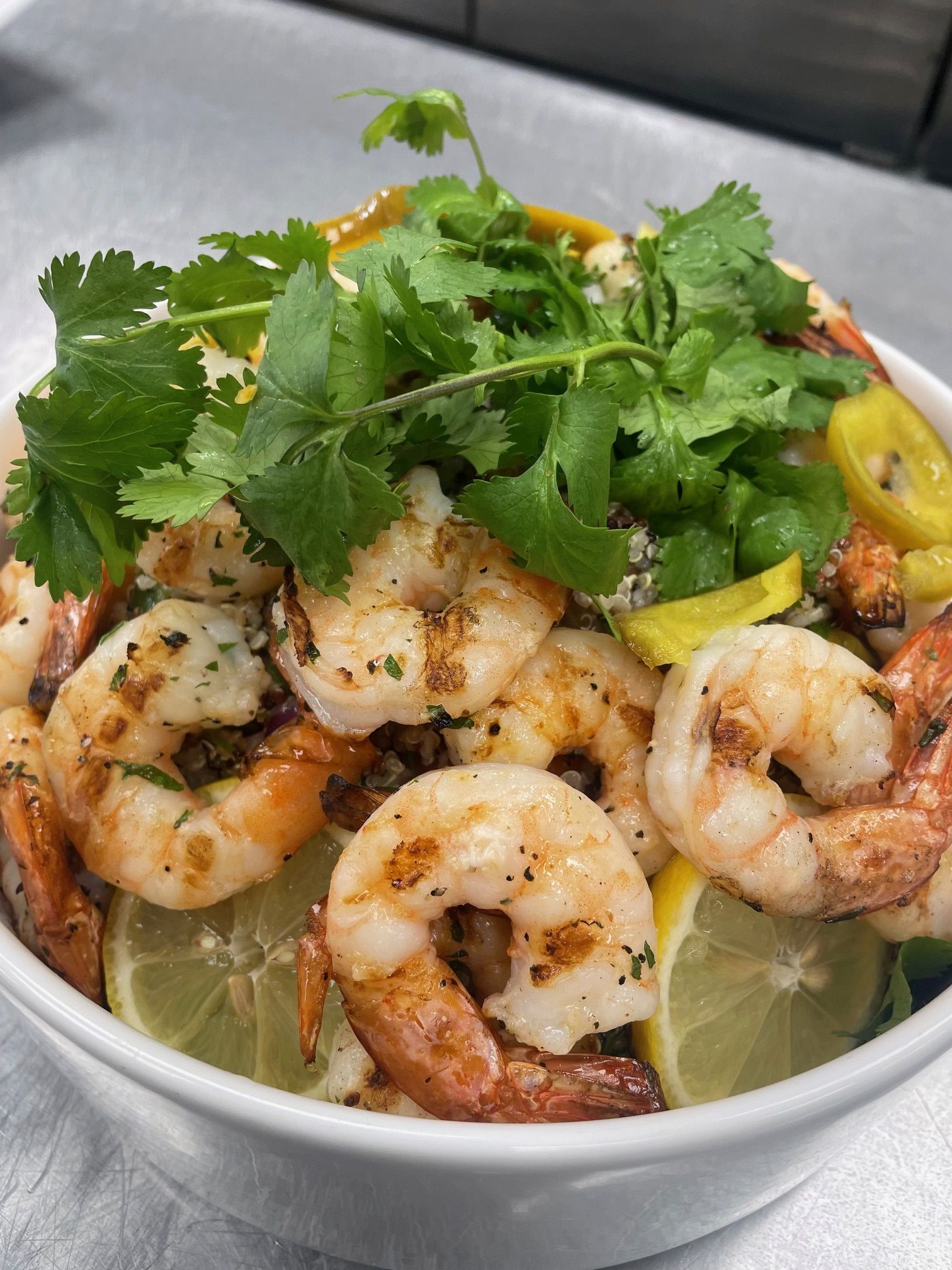 A bowl of shrimp , cilantro , lemon slices and peppers on a table.