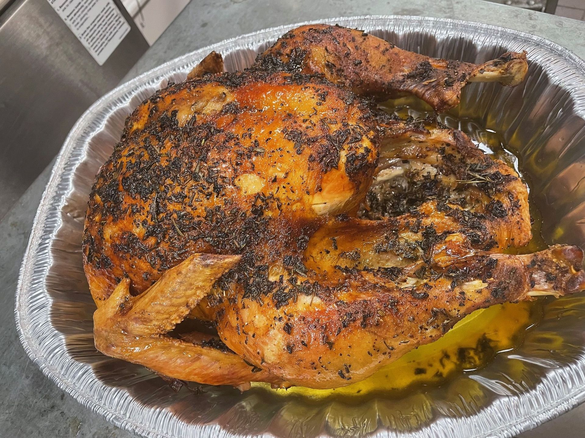 A roasted chicken is in a tin foil pan on a table.