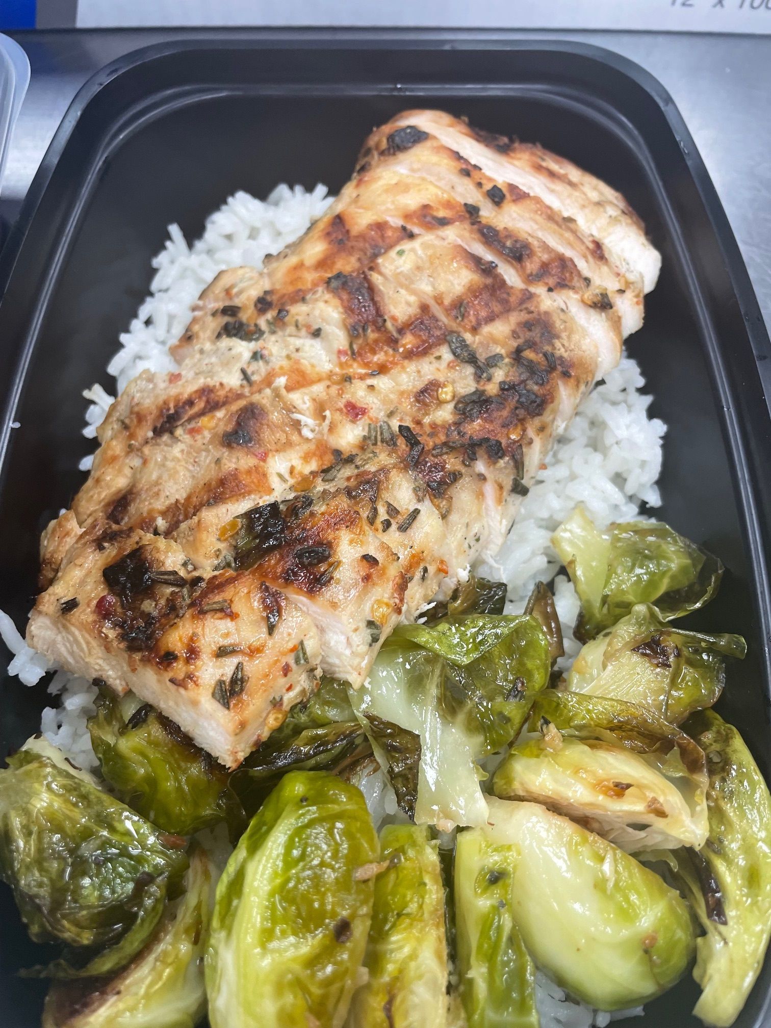 A black container filled with rice , chicken , and brussels sprouts.