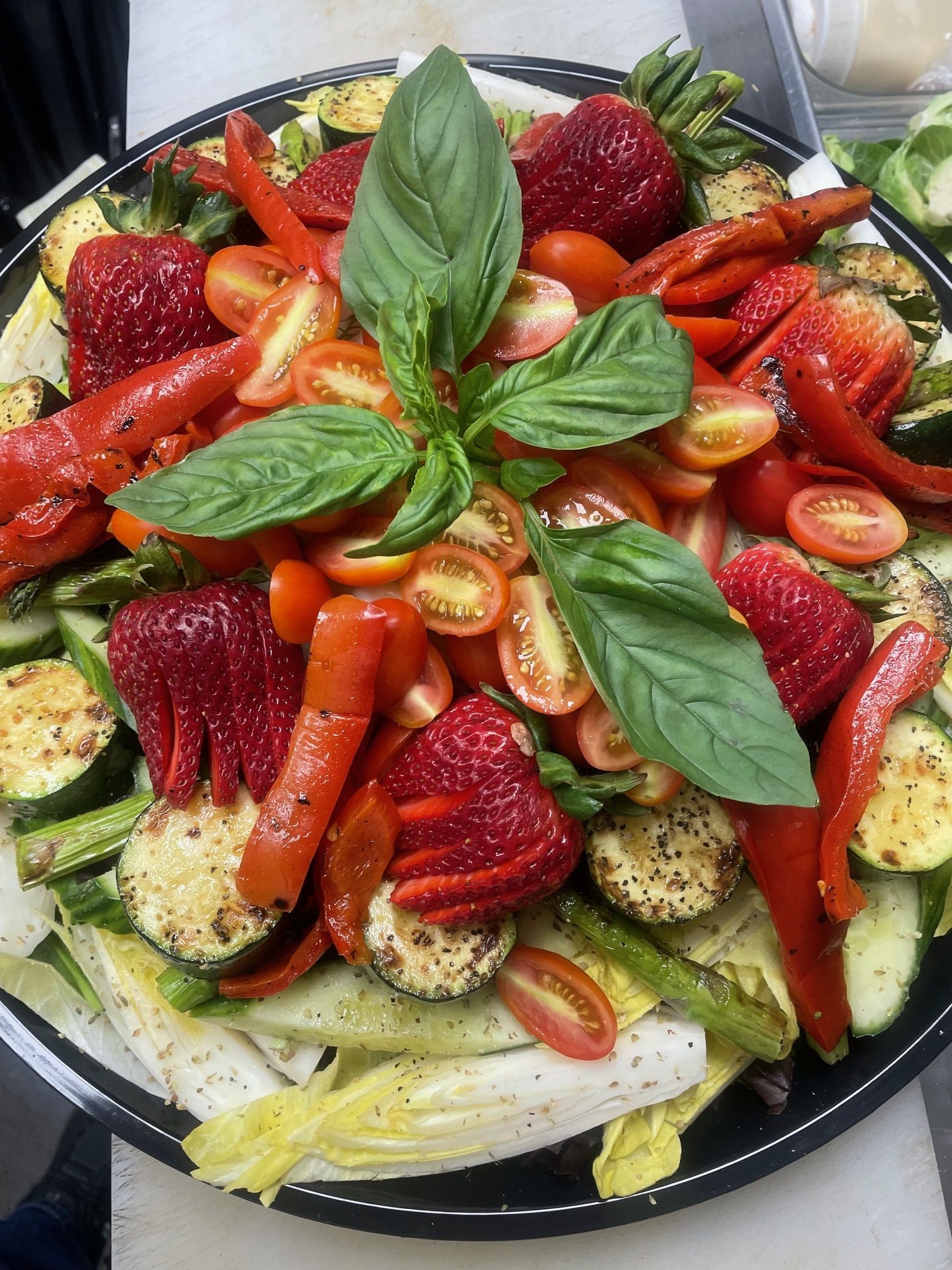 A plate of vegetables with strawberries and basil on top.
