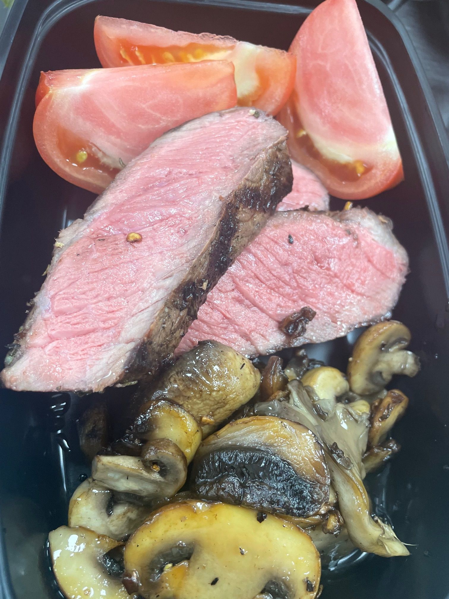 A close-up of a plate of food with meat, mushrooms, and tomatoes.
