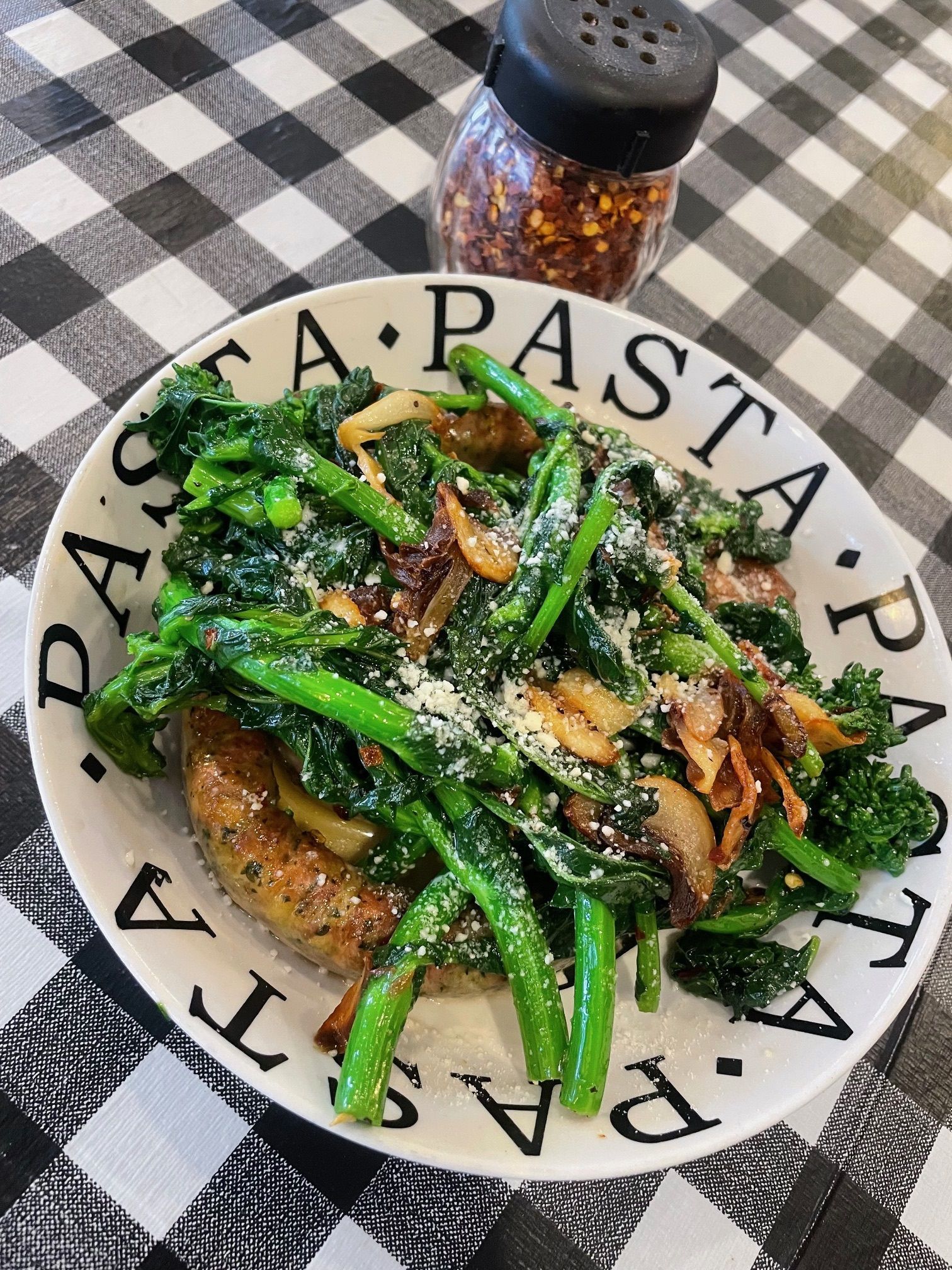 A plate of pasta with broccoli and mushrooms on a checkered table cloth.