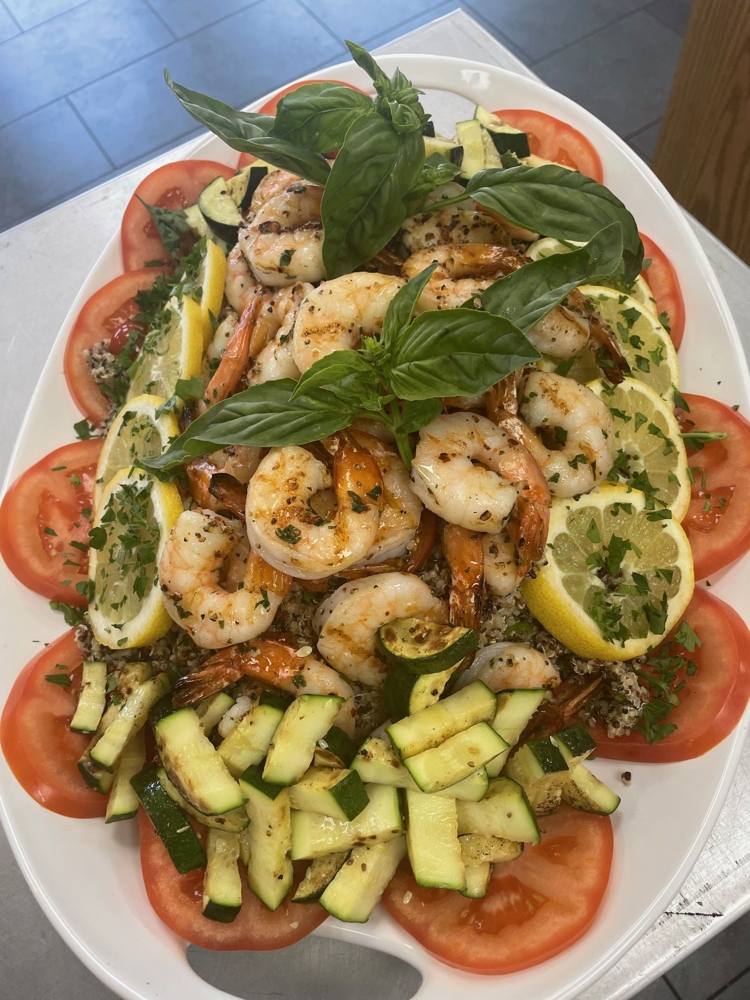 A white plate topped with shrimp , tomatoes , lemons and zucchini.