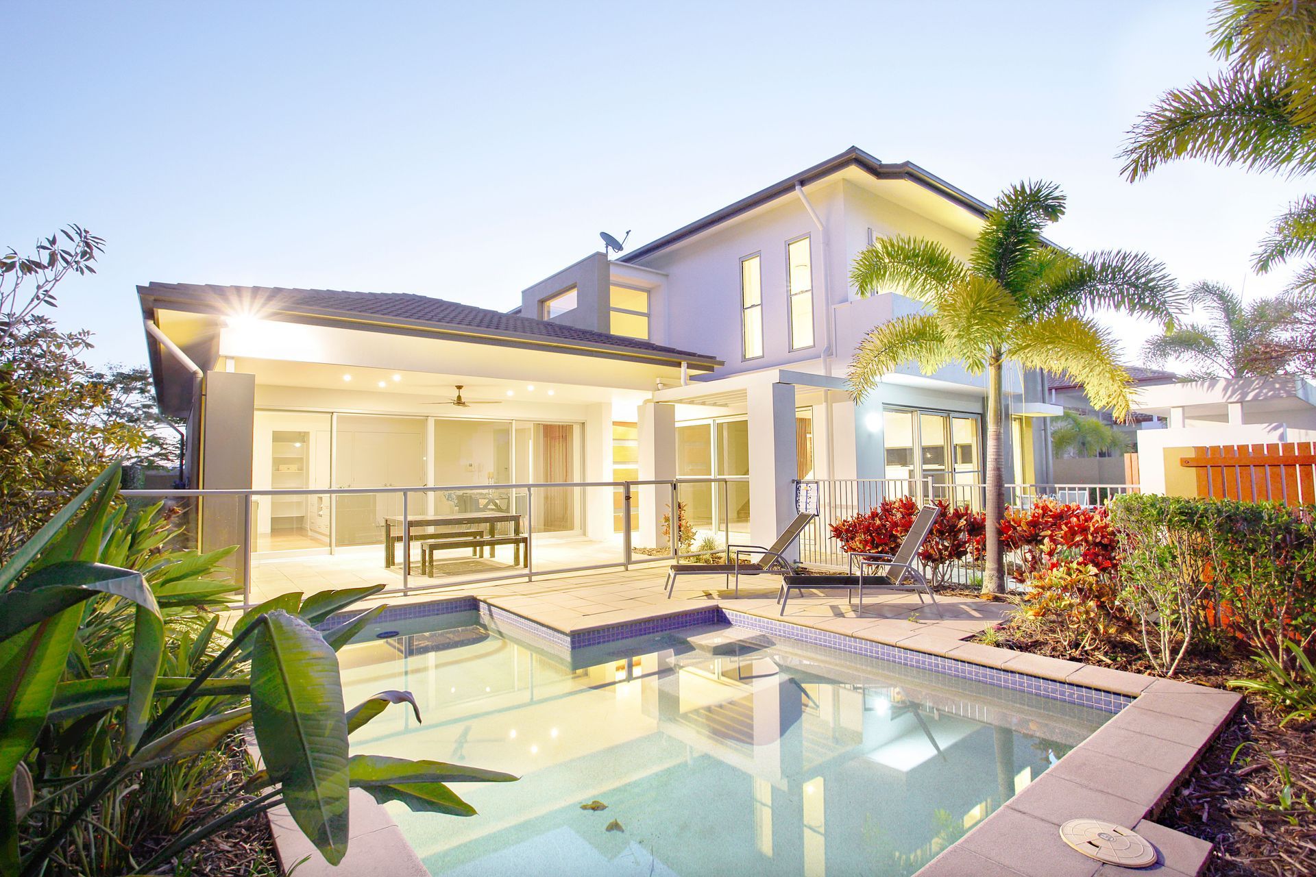 Luxury two-story house with a lit patio and backyard swimming pool at dusk