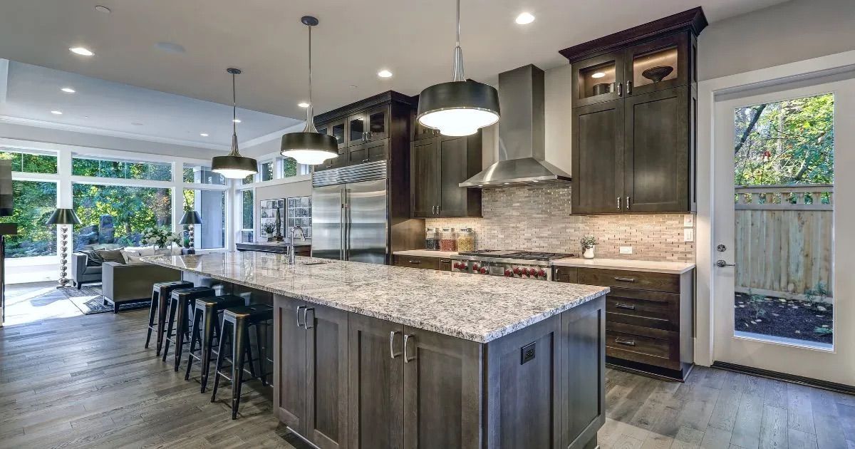 Modern kitchen with large granite island, dark cabinets, pendant lights, and open view to patio and yard