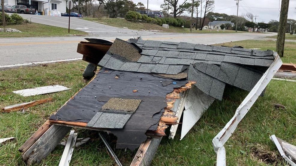 Collapsed roof shingles and debris lying on a lawn beside a street after storm damage