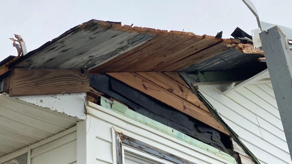 Damaged roof with torn shingles and exposed wood on a white house corner