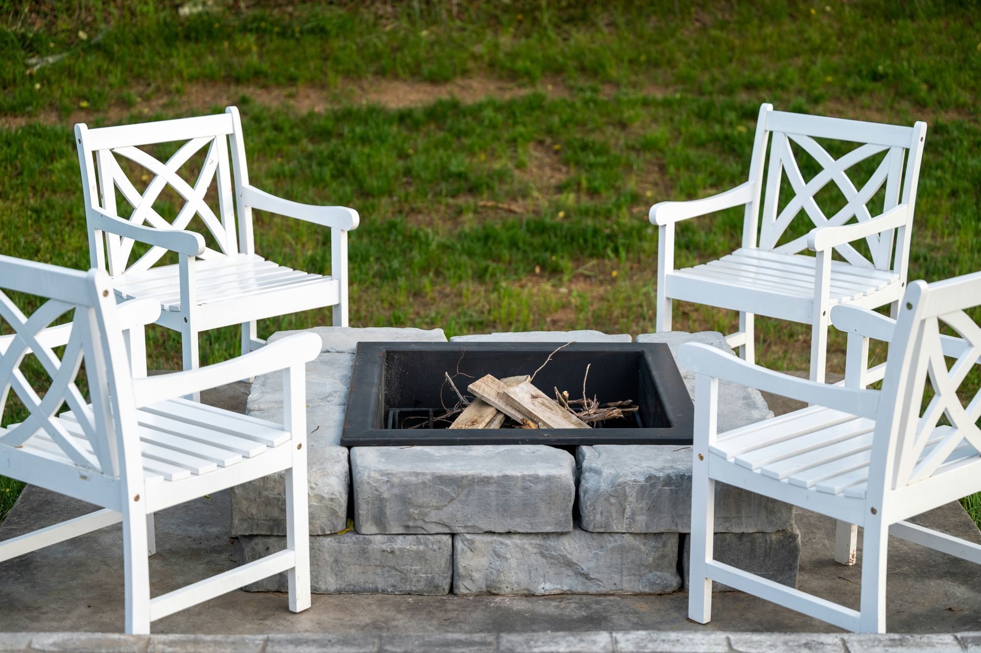 White chairs arranged around a stone fire pit on a patio with grass in the background