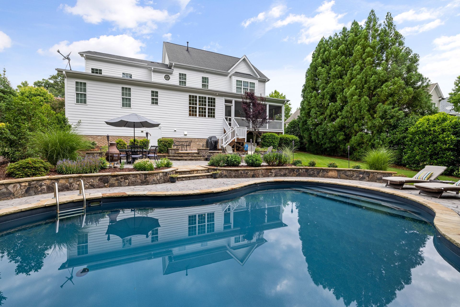 White house with a large backyard pool and landscaped garden under a blue sky