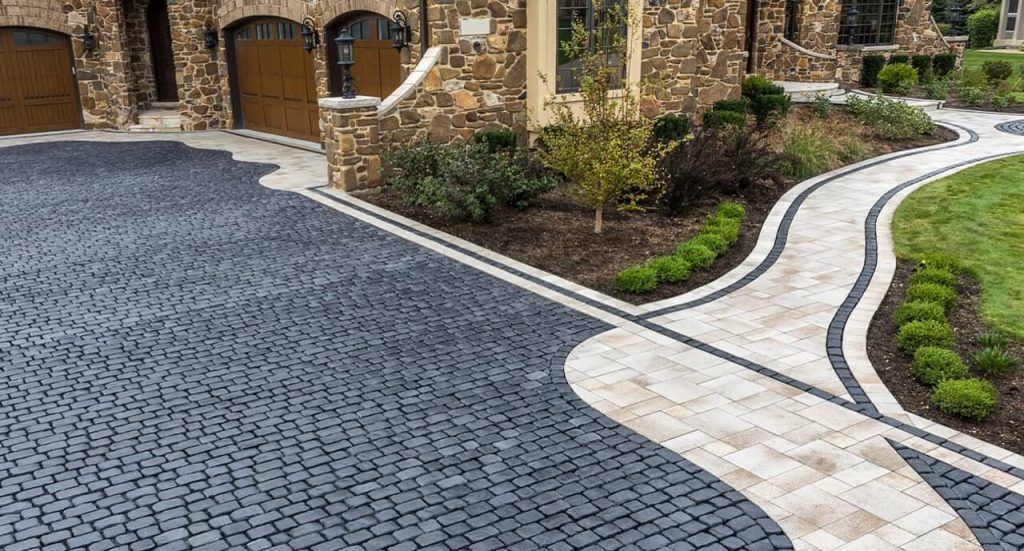 Curved cobblestone driveway beside a stone house and landscaped garden path