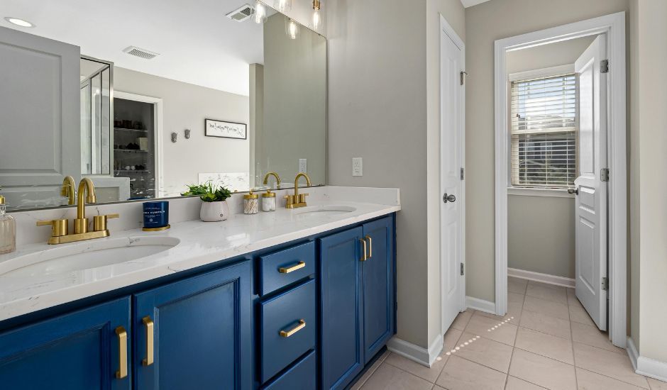 Bright bathroom with blue vanity, large mirror, and tiled floor leading to a closet or water closet.