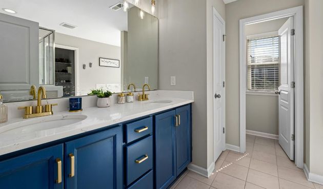 Bright bathroom with blue vanity, large mirror, and tiled floor leading to a closet or water closet.