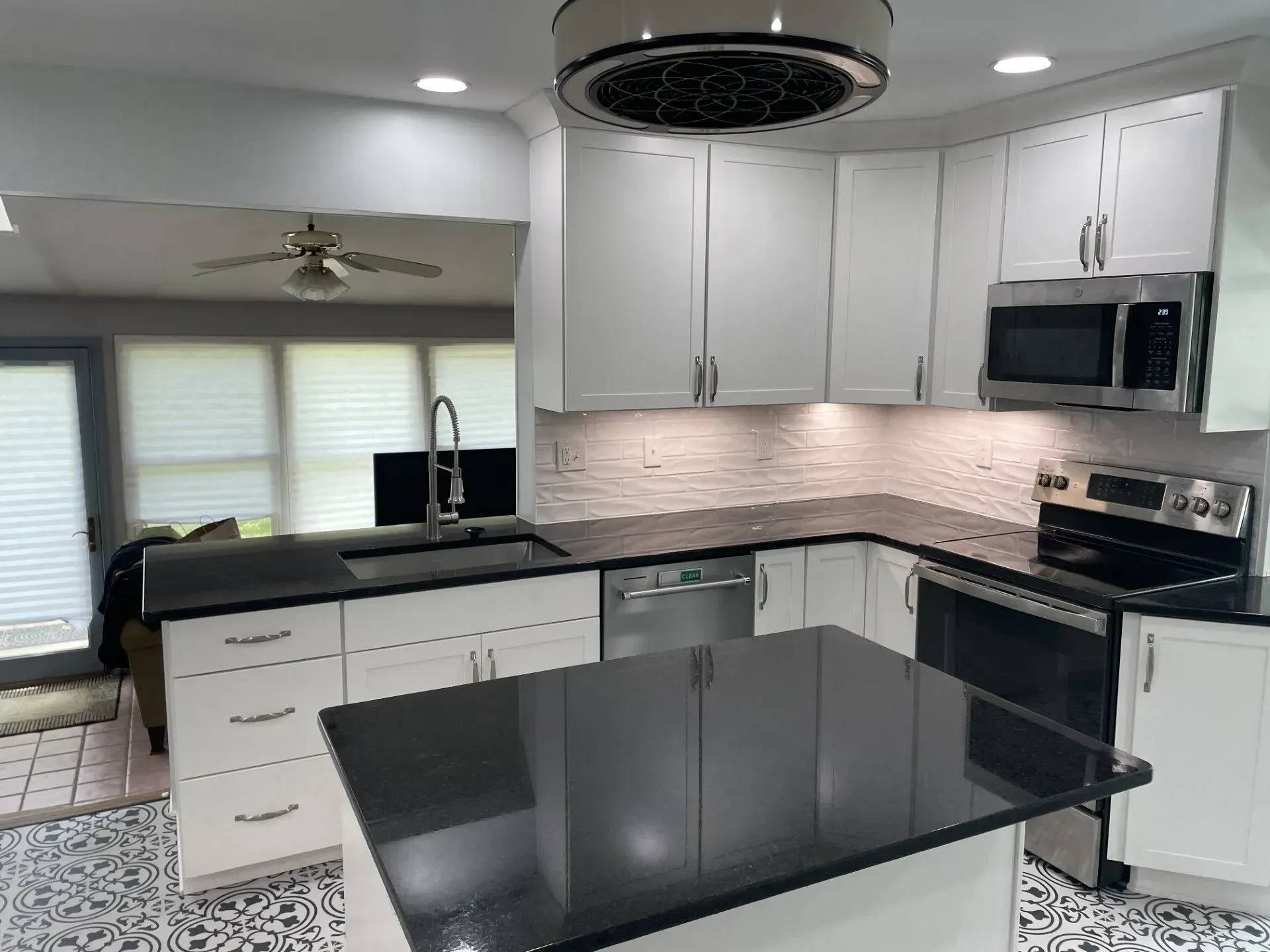 A kitchen with white cabinets , black counter tops , stainless steel appliances and a large island.
