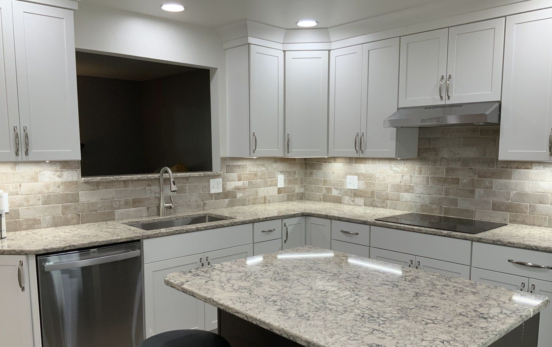 A kitchen with white cabinets , granite counter tops , stainless steel appliances and a large island.