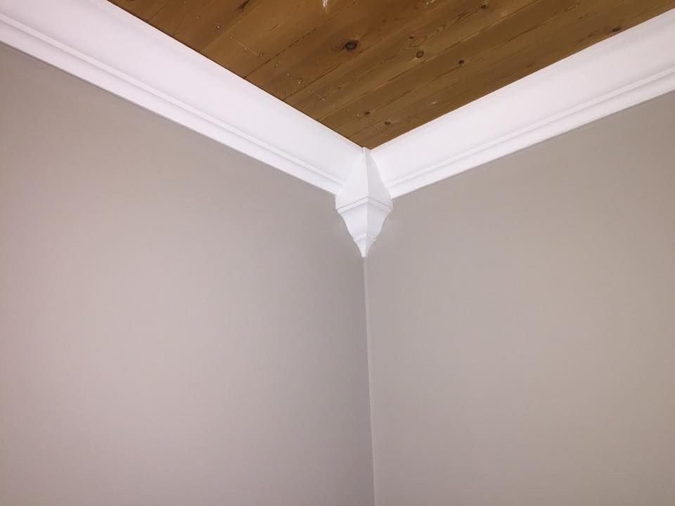 A corner of a room with white trim and a wooden ceiling.